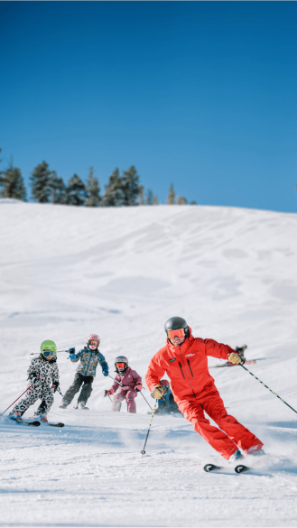 Ski pro at Aspen carves down slope followed by 4 young kids