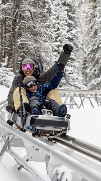 father and son on alpine coaster at snowmass in the wintery, snow covered trees 