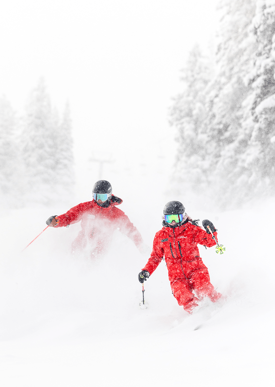 two aspen snowmass ski pros carve through powder on a snowy day in Aspen