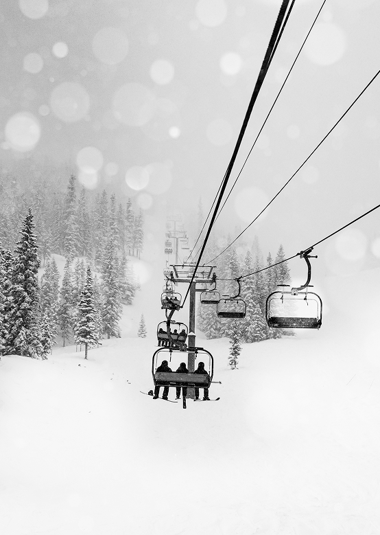 black and white image of snow falling on powder packed hills as a chairlift of guests get ready to ski powder