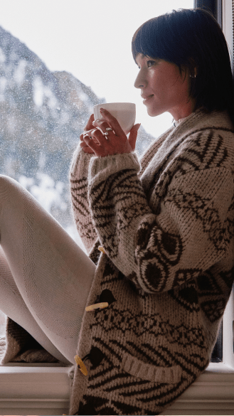 Woman drinking from steaming mug wearing aspen collection sweater