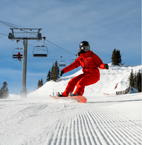 snowboarder carves through groomed snow under lift at Aspen Highlands