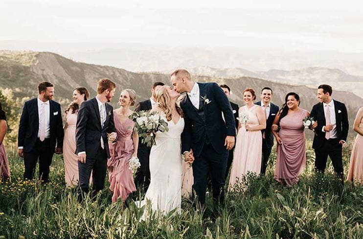 Couple kisses in meadow with wedding party at Snowmass