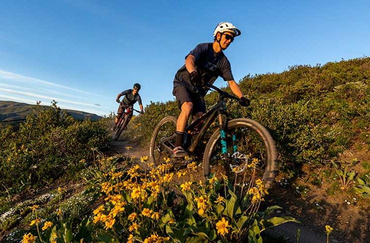 Two riders on a cross-country mountain bike trail at sunset