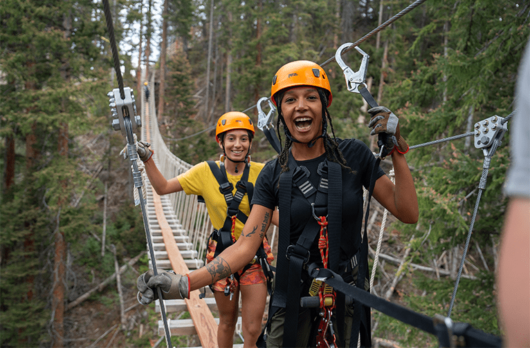 Two girl smile as they cross a hanging bridge at Lost Forest in Snowmass