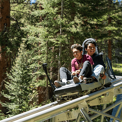 Two young boys on the alpine coaster, smiling out of excitement at Snowmass Lost Forest