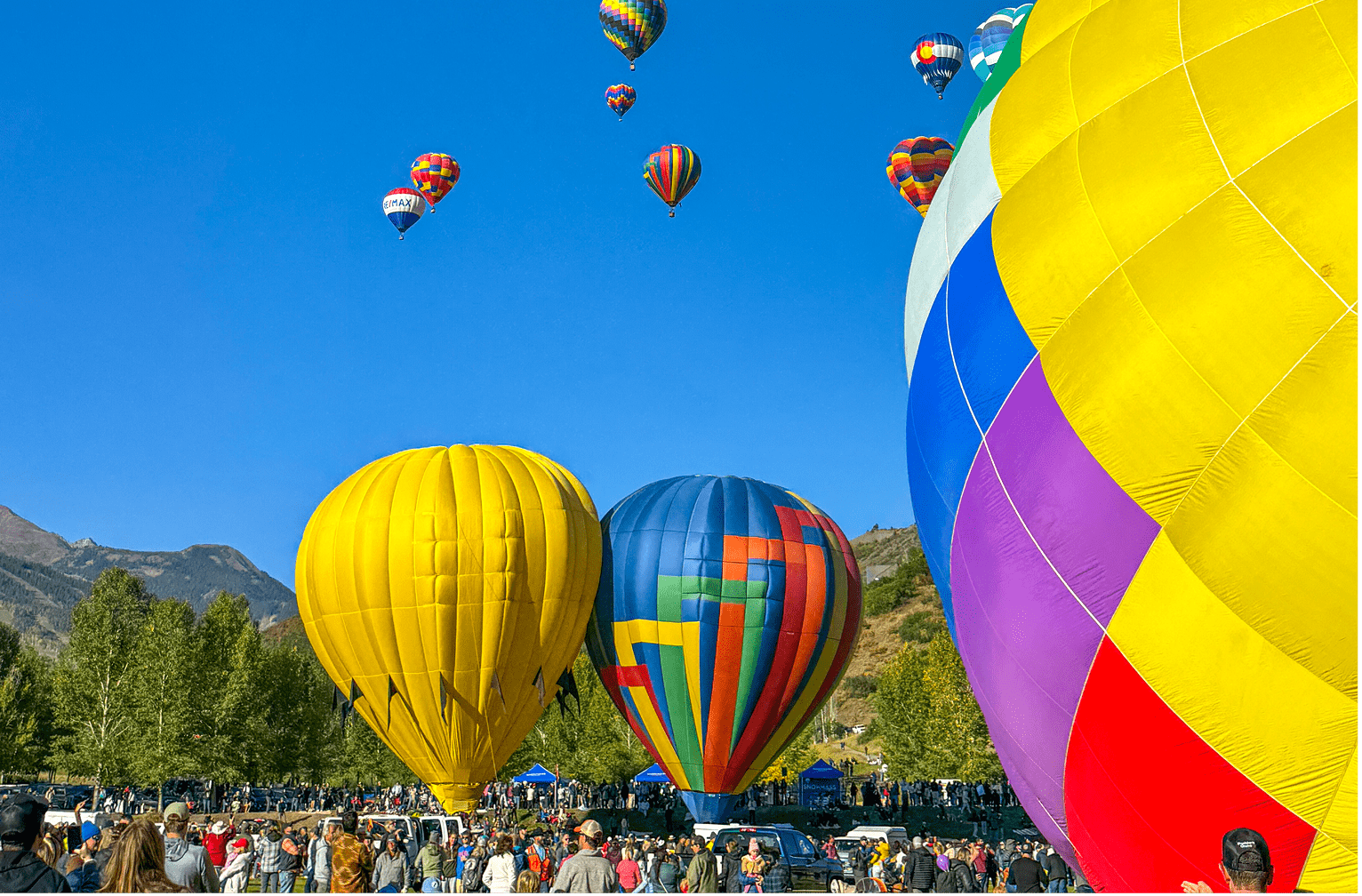 hot air balloons raise from a field in snowmass, as many balloons float in the ski in the distance