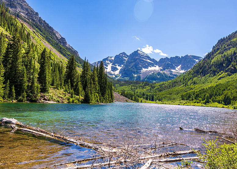 Maroon Bells on a sunny summer day, blue sky reflects off the vibrant blue lake at the base of the Maroon Bells, which still have a dusting of snow