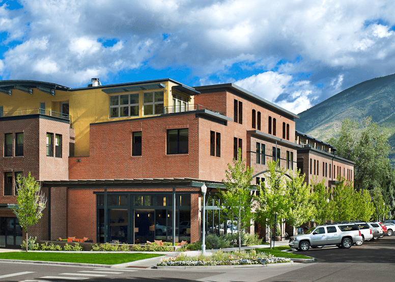 Exterior of the Limelight Aspen, on a summer day, green mountains behind hotel and blue sky above