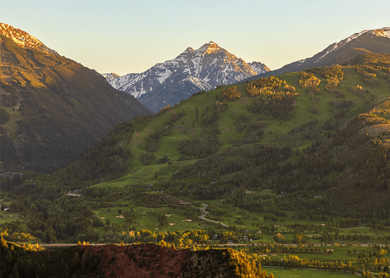 Buttermilk mountain at dusk, sun sets golden hue pm green grass ski slope