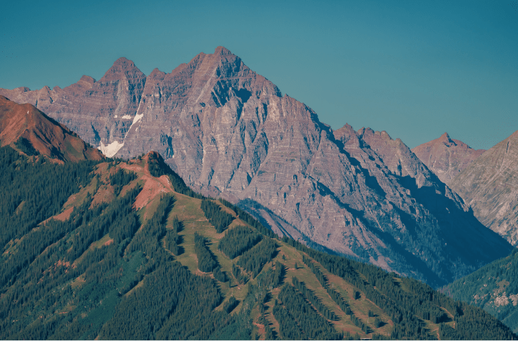 Birds eye view of aspen highlands in summer, with stark peaks behind green ski runs