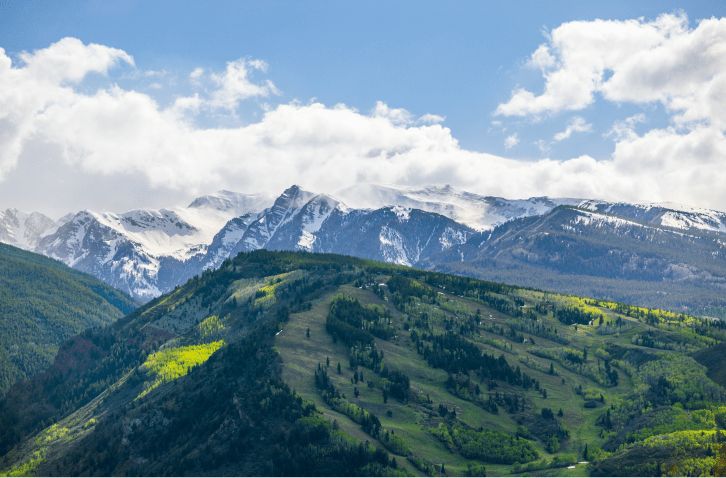 Aerial view of buttermilk mountain, green with spring colors, snow still on peaks behind