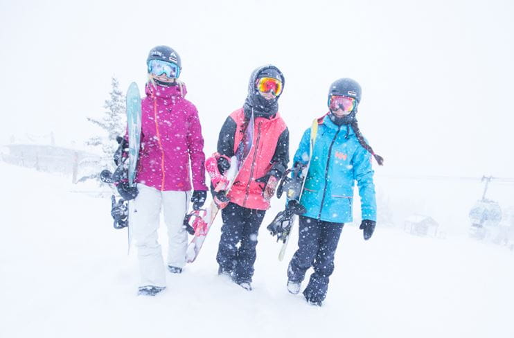 A group of women snowboarders walking through a light snow