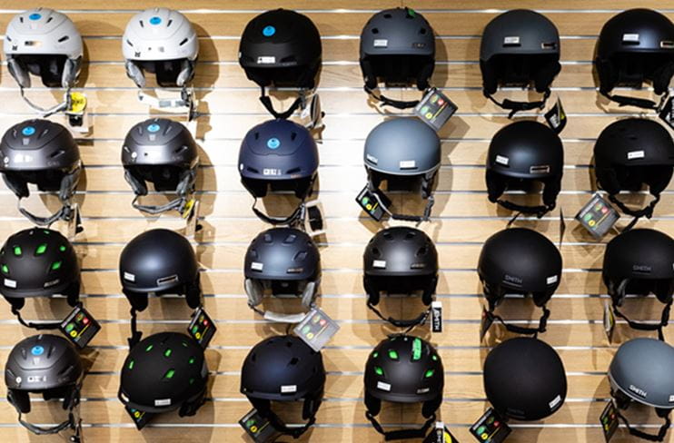 A variety of ski and snowboard helmets for sale are displayed on a wall.