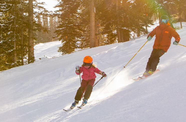 A child learns to ski with an adult instructor