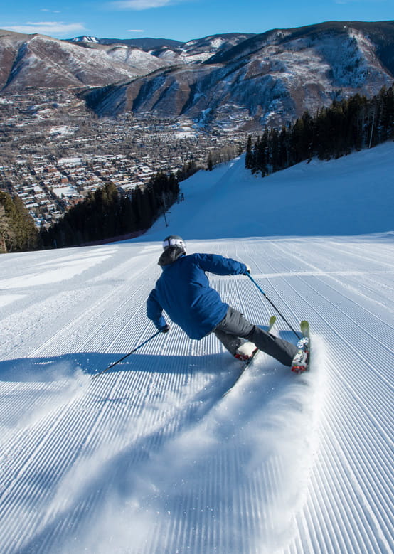 A skier in a blue ski jacket starts his journey down a freshly groomed mountain in Aspen.