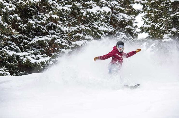 A snowboarder carves through powder at Aspen Mountain