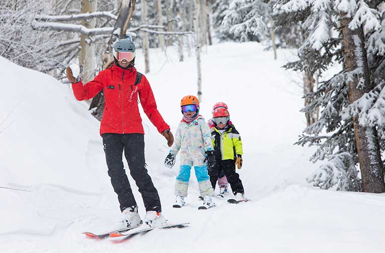 A ski instructor leads kids down a trail at Snowmass
