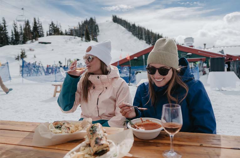 two women sitting at a table with food and drinks