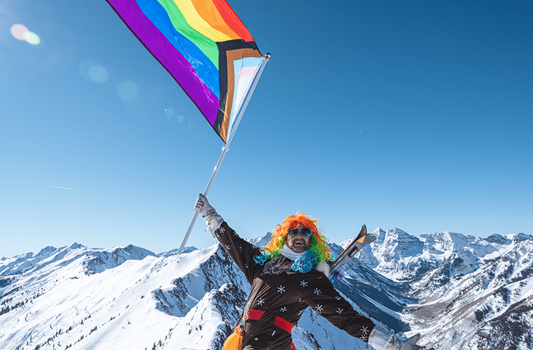 Gay Ski Week participant on top of Highlands with LGBTQ+ flag at aspen Snowmass