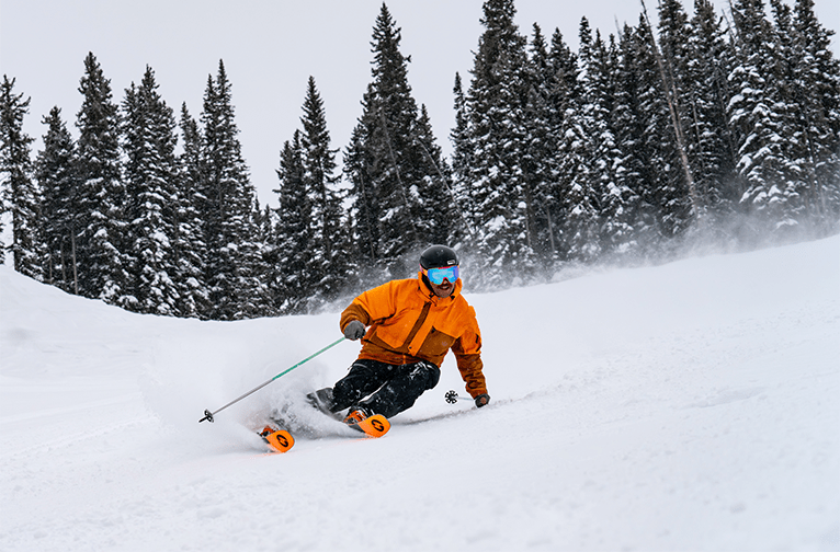 Skier in a bright orange jacket carves down groomer on an overcast day