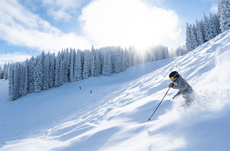 Skier on Aspen Mountain, blue bird day with fresh powder, snowy trees in background