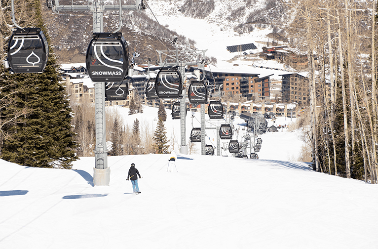 Skier benieth the Snowmass gondola, on a bluebird day, and they cruise down a groomer