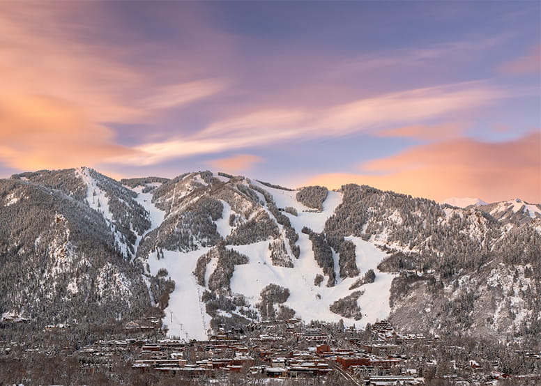 Snow-covered mountain slopes form ski trails, descending toward a village nestled below.