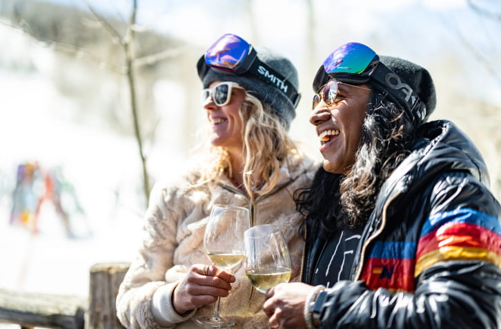 Two people laughing and smiling with glasses of wine at a mountain restaurant