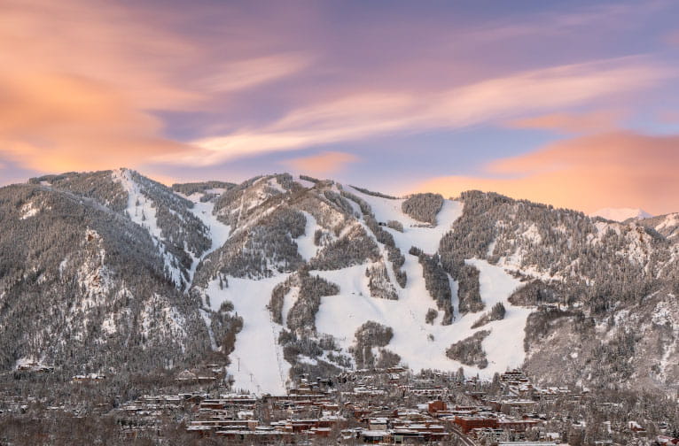 Snowy mountains stand under a vibrant sky, with ski trails visible above a quaint town.