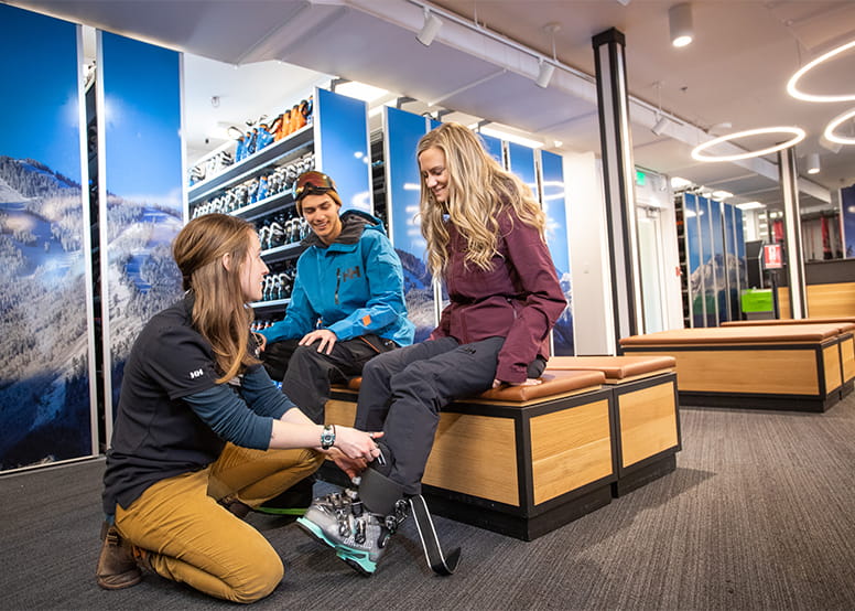 A couple sits in four mountain sports while they get their boots fitted for a day at Aspen Snowmass