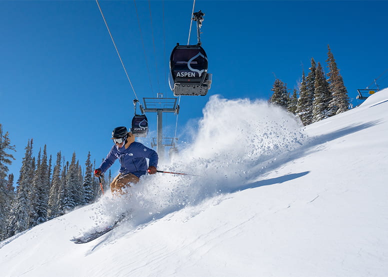 Skier carves through powder under the Aspen Silver Queen Gondola 