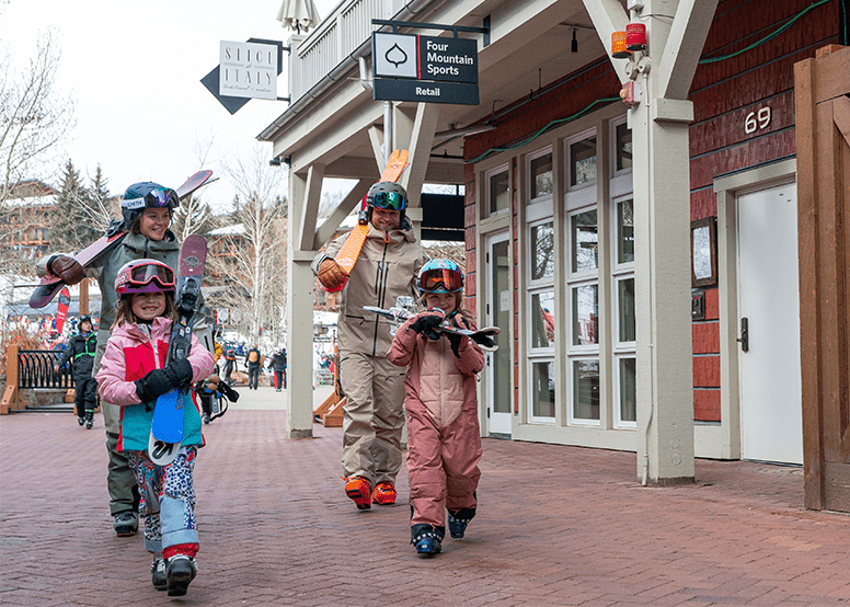 Family of four walks through the Snowmass mall, laughing, as they carry their skies on their shoulders