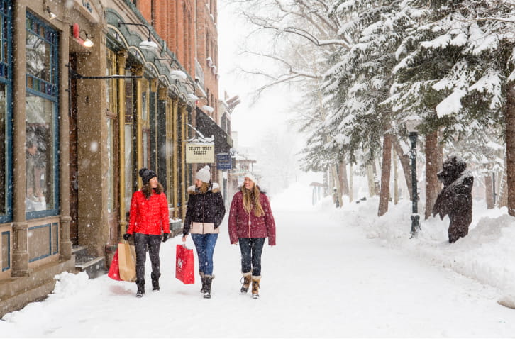 3 people walking in Downtown Aspen with shopping bags during the snow in winter