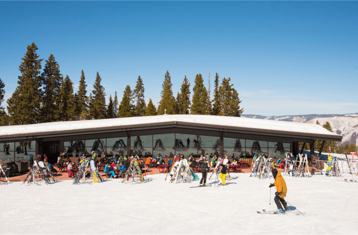Exterior view of Merry Go Round, people ski to entrance and others sit outside in the sun
