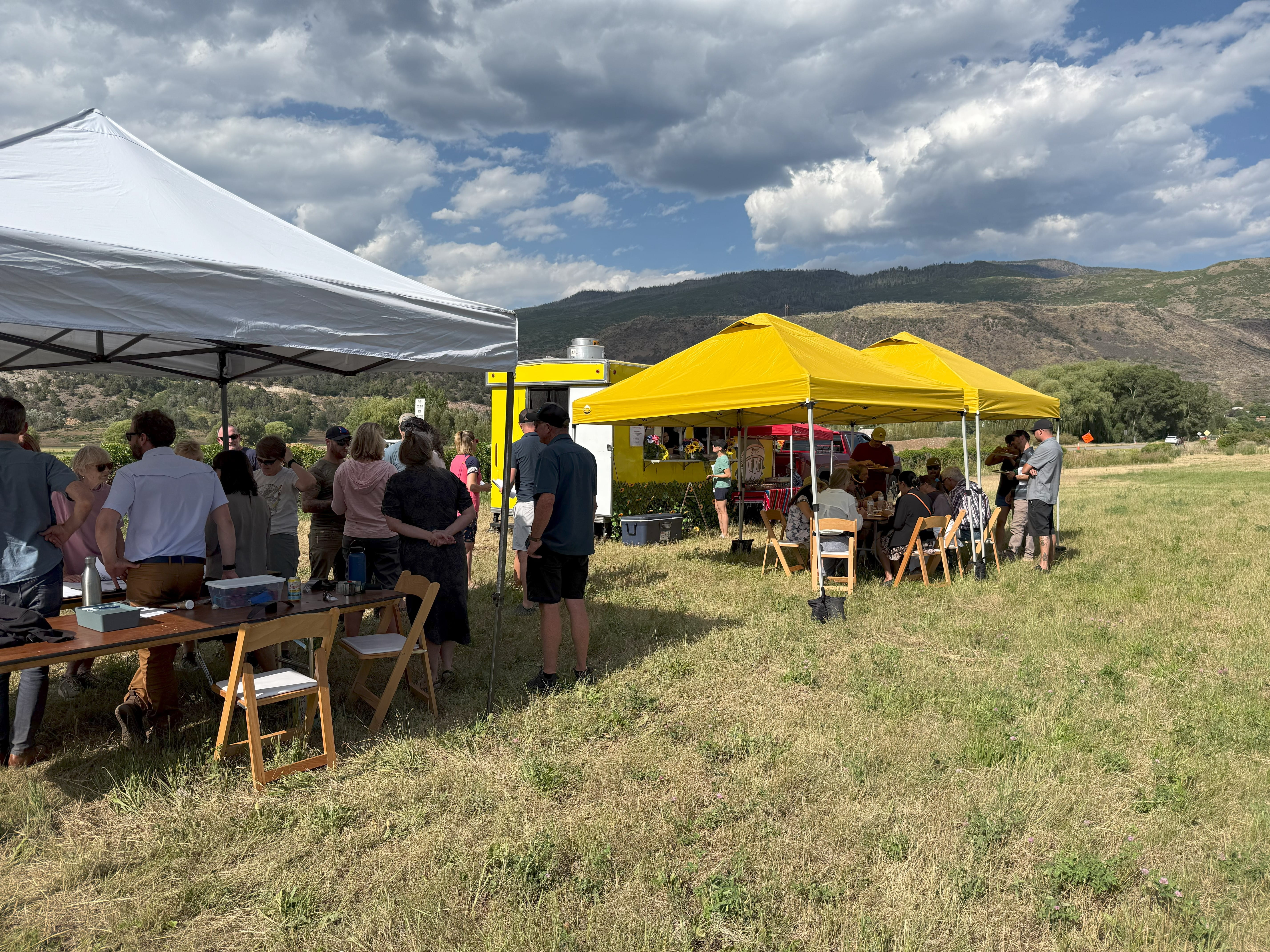 people gather outside in a field under yellow and white tents
