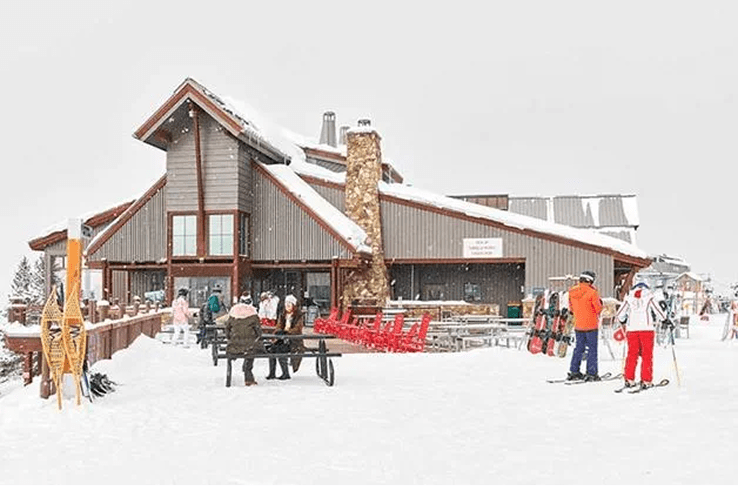 Sundeck in the winter, snow falls around the gray cabin, skiers stand outside