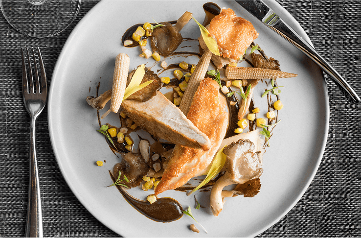 Chicken fillets skillfully plated on white plate with sauce, and seasonal greens
