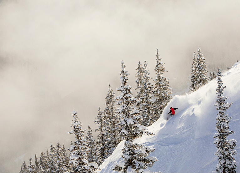 Single skier on ridge of ski hill, fog and clouds behind the powder-y hill