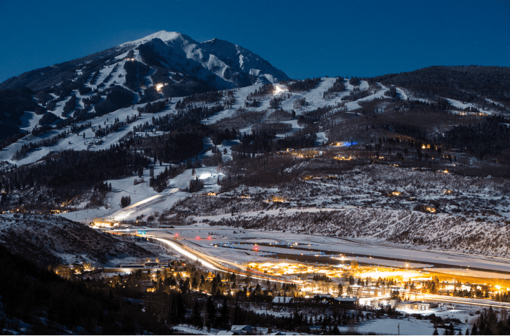 Aspen snowmass airport at night, runway lights shine in the snow as a blue black screen sets over the mountains