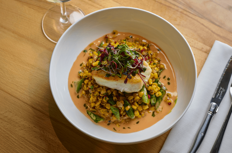 A bowl of corn chowder topped with Halibut and fresh greens