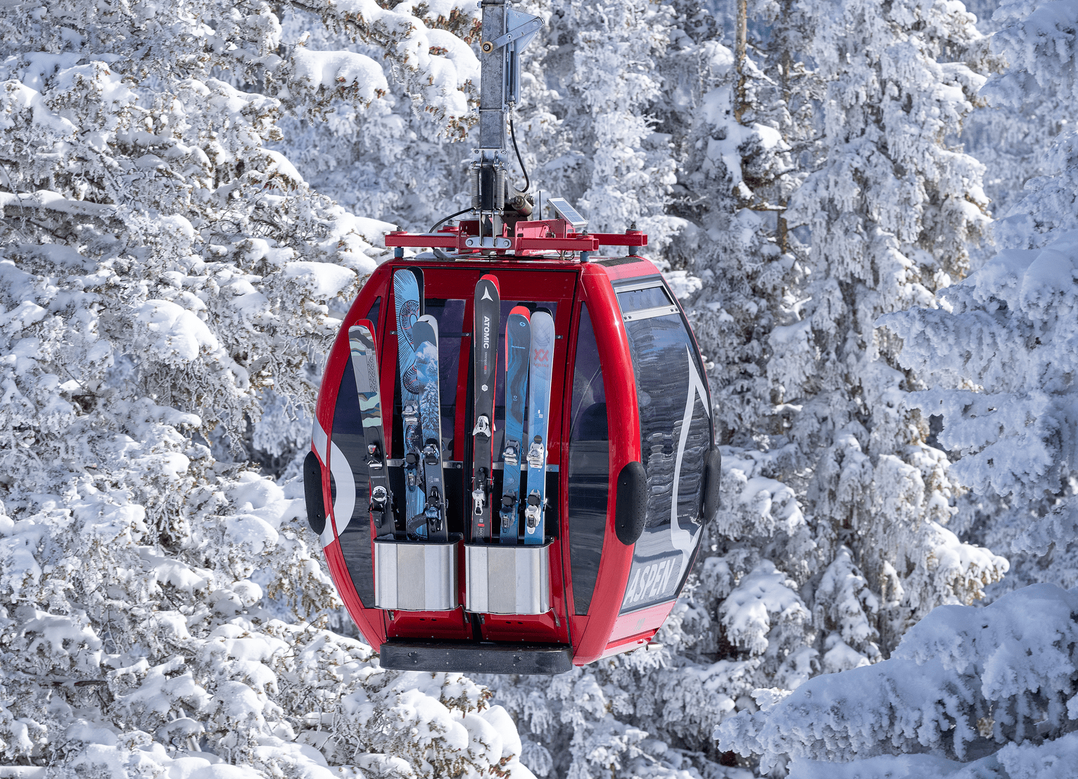 Red gondola car in front of snowy trees, skies and snowboards packed in the gondola car