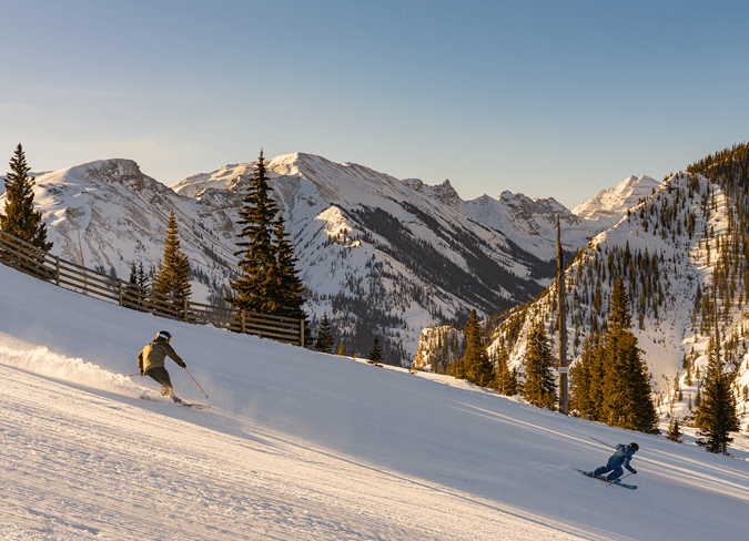 two skiers carve down an empty groomed run during sunset skiing at aspen snowmass