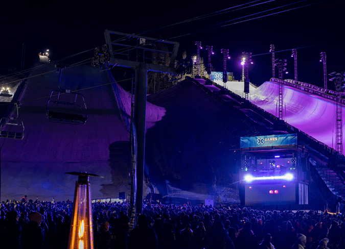 Illuminated half pipe at the xgames, purple lighting lights up the crowd below