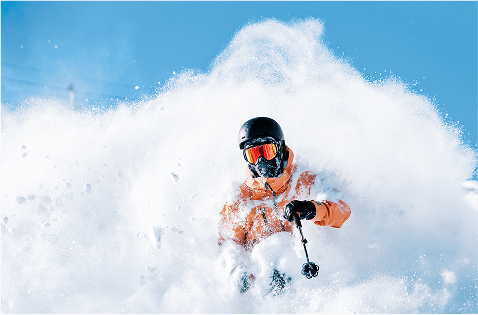 Person emerges through a cloud of powder, on a blue bird day in their orange ski jacket, at aspen snowmass
