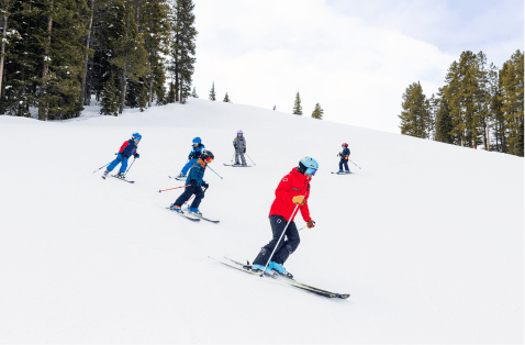 Group of kids follow in single file line down Aspen mountain during a ski lesson
