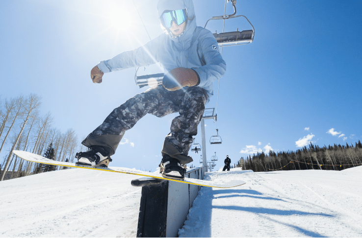 Kid on snowboard goes off a box in the terrain park during his lesson at Aspen Snowmass