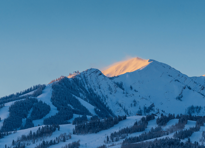 blue light over the runs at aspen highlands, as the sun hits the bowl and casts an orange light over the snow