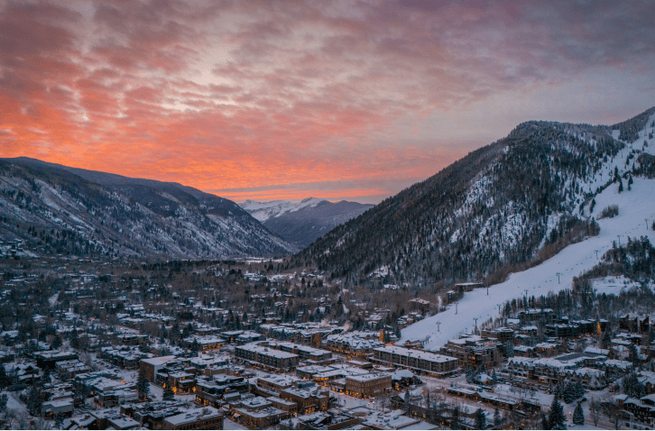 Sunset over the down of aspen, pink clouds streak the sky as the town, covered in slow, sits below the ski runs
