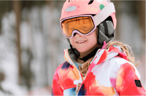 little girl smiles in her ski helmet and goggles, as she prepares to ski at aspen snowmass